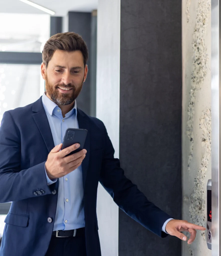 Caucasian man in blue suit on his smartphone pushing the elevator button