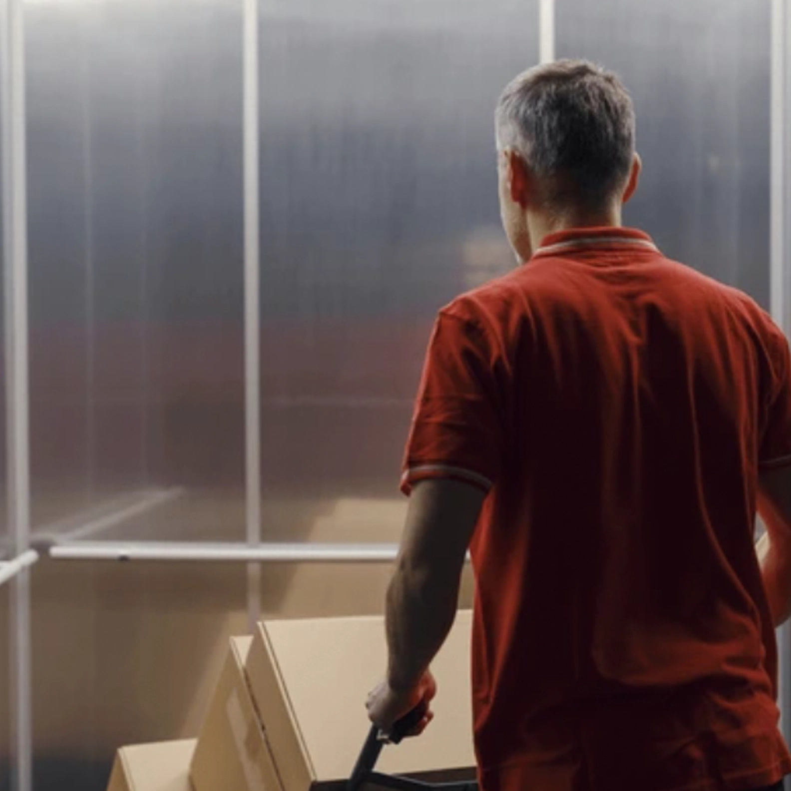 Delivery person entering elevator with dolly of parcels