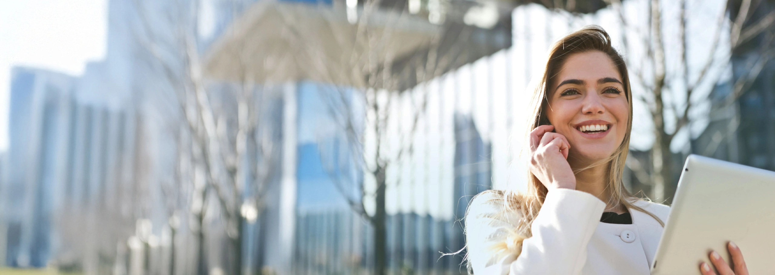 Woman talking on the phone while holding a tablet outside in front of a commercial building
