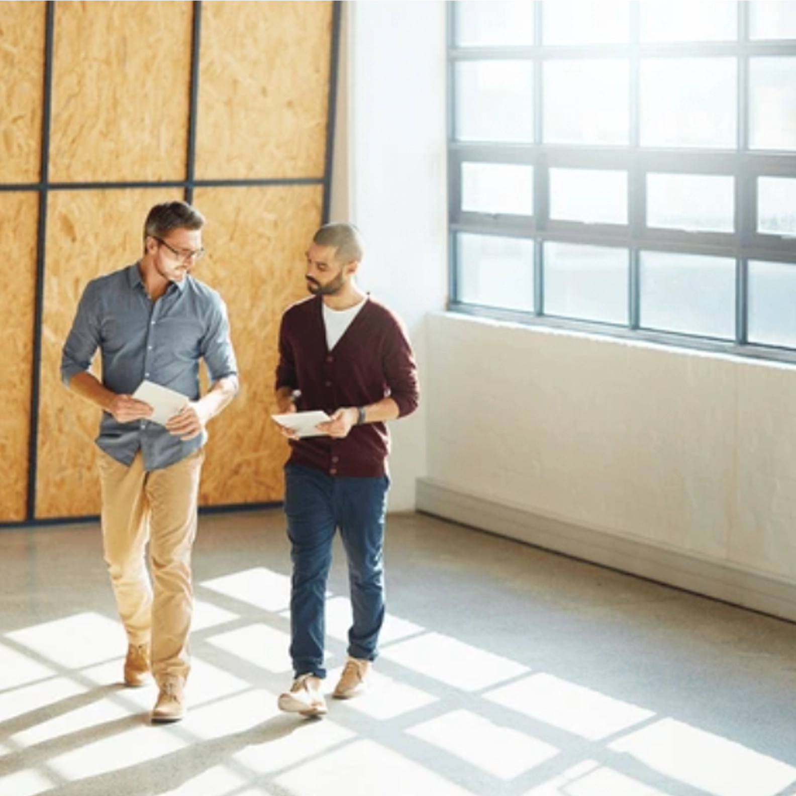 Two men walking in an empty room with a large window