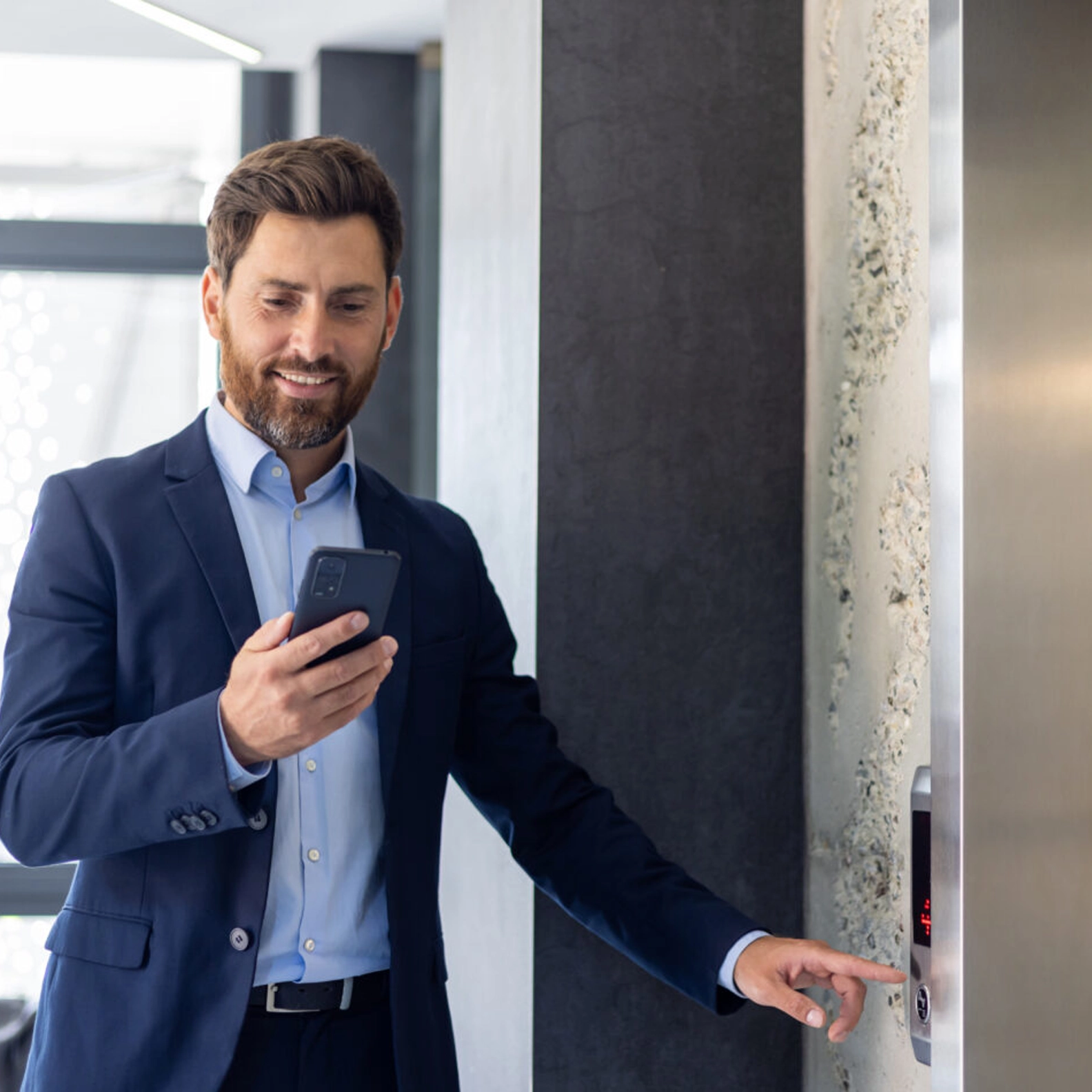 Man pushing an elevator button while using his smart phone