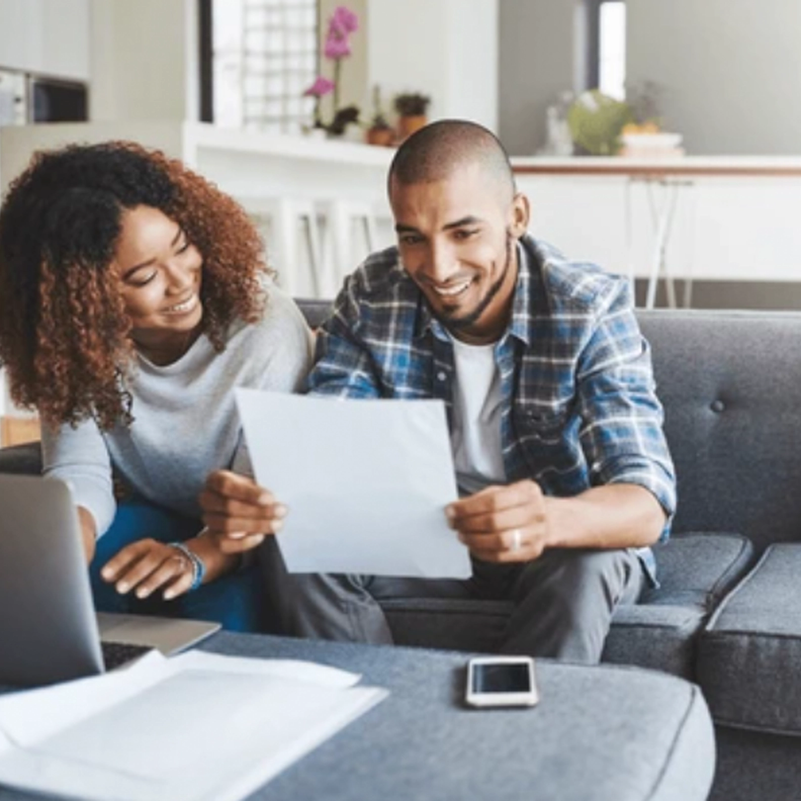 Couple reviewing paperwork while using their laptop on their sofa